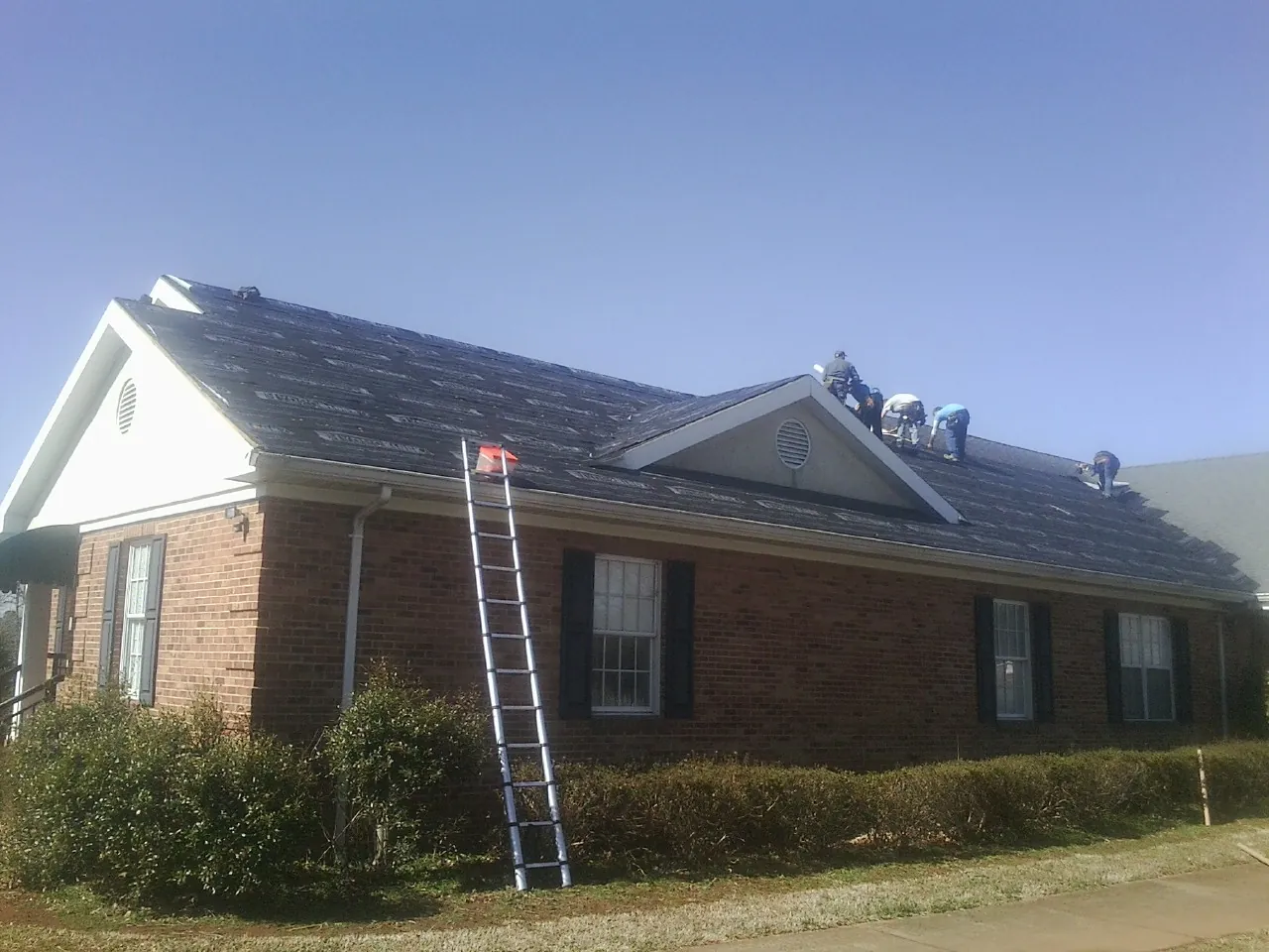 Crew tearing shingles off a brick ranch roof with a ladder set — Metal Roof Repair work by our crew in Blounts Creek