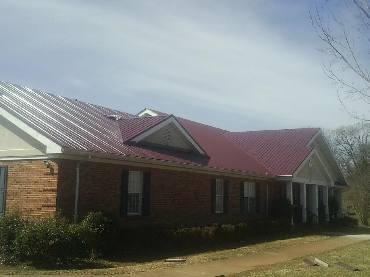 Red metal roof with gabled entries on a long brick building, from a Hail Damage Roof Repair job in Blounts Creek