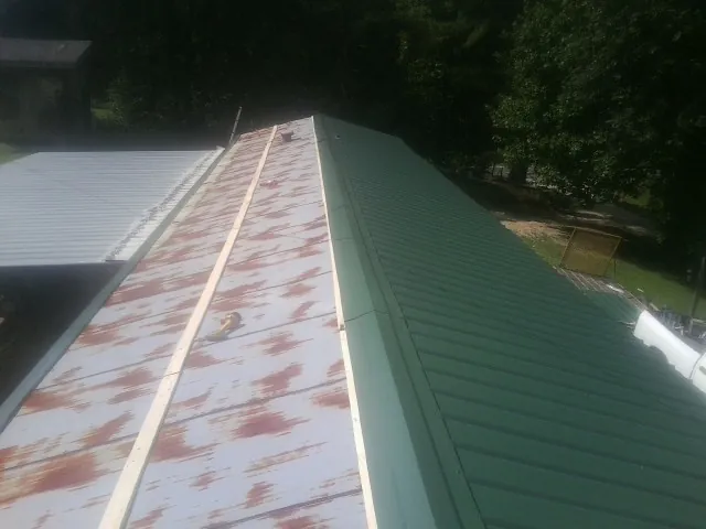 Old rusted panels beside newly installed green metal roofing — Wind Damage Roof Repair by Roofing Brothers in Blounts Creek