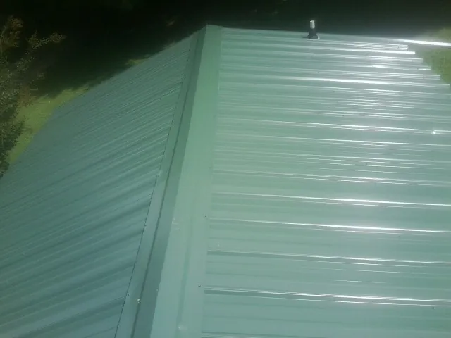 New green metal panels meeting at the ridge of a roof — Flat Roof Repair work by our crew in Blounts Creek
