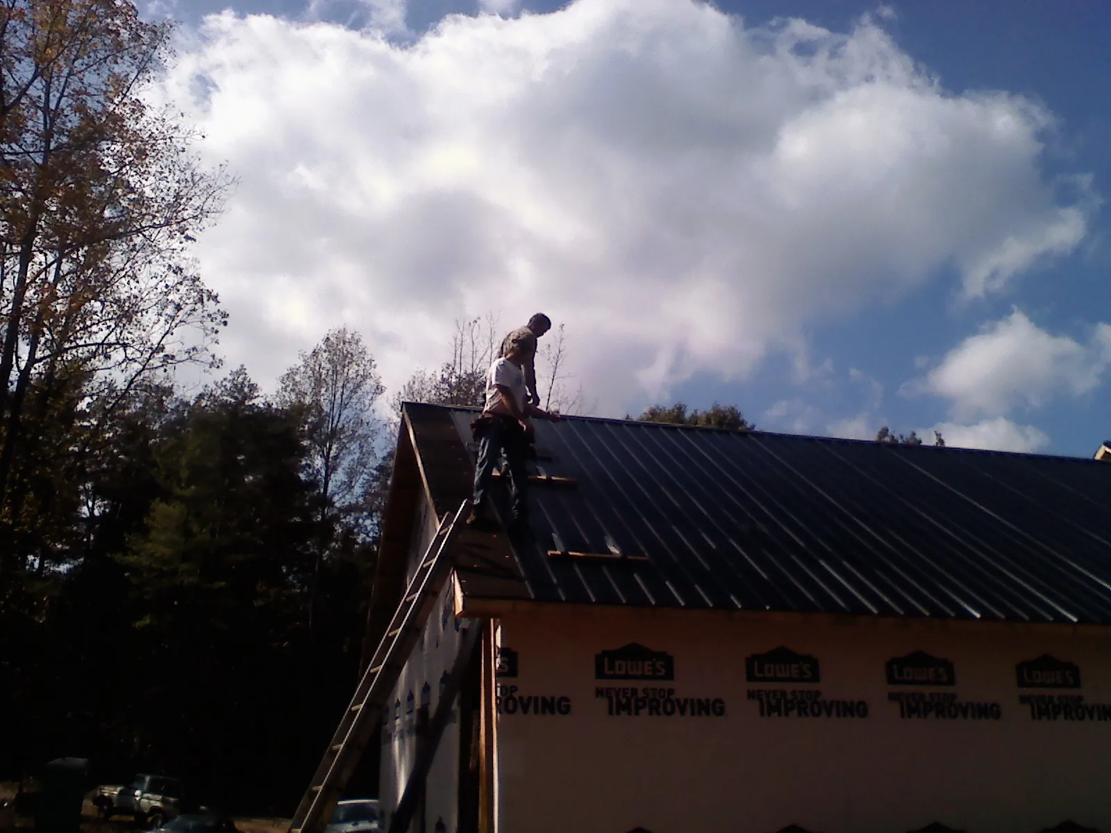 Roofer fastening dark metal panels high against a cloudy sky, from a Roof Inspection job in Blounts Creek