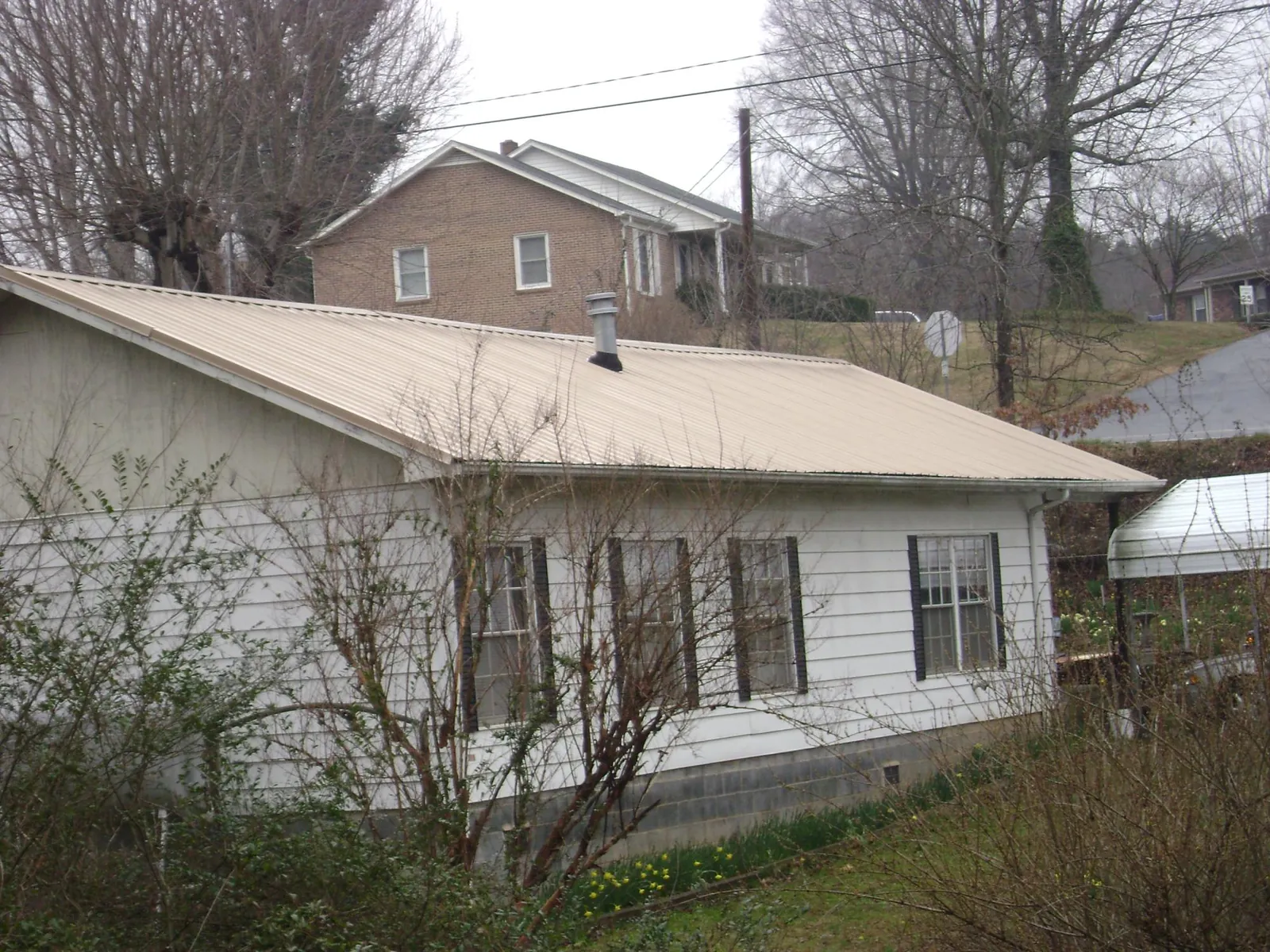 Tan metal roof on a white sided house set into a hillside — Commercial Roofing by Roofing Brothers in Blounts Creek